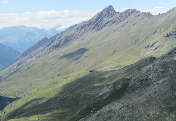 paesaggio montano con al centro un rifugio a cui giunge un sentiero. dietro la punta del Pic Traverse