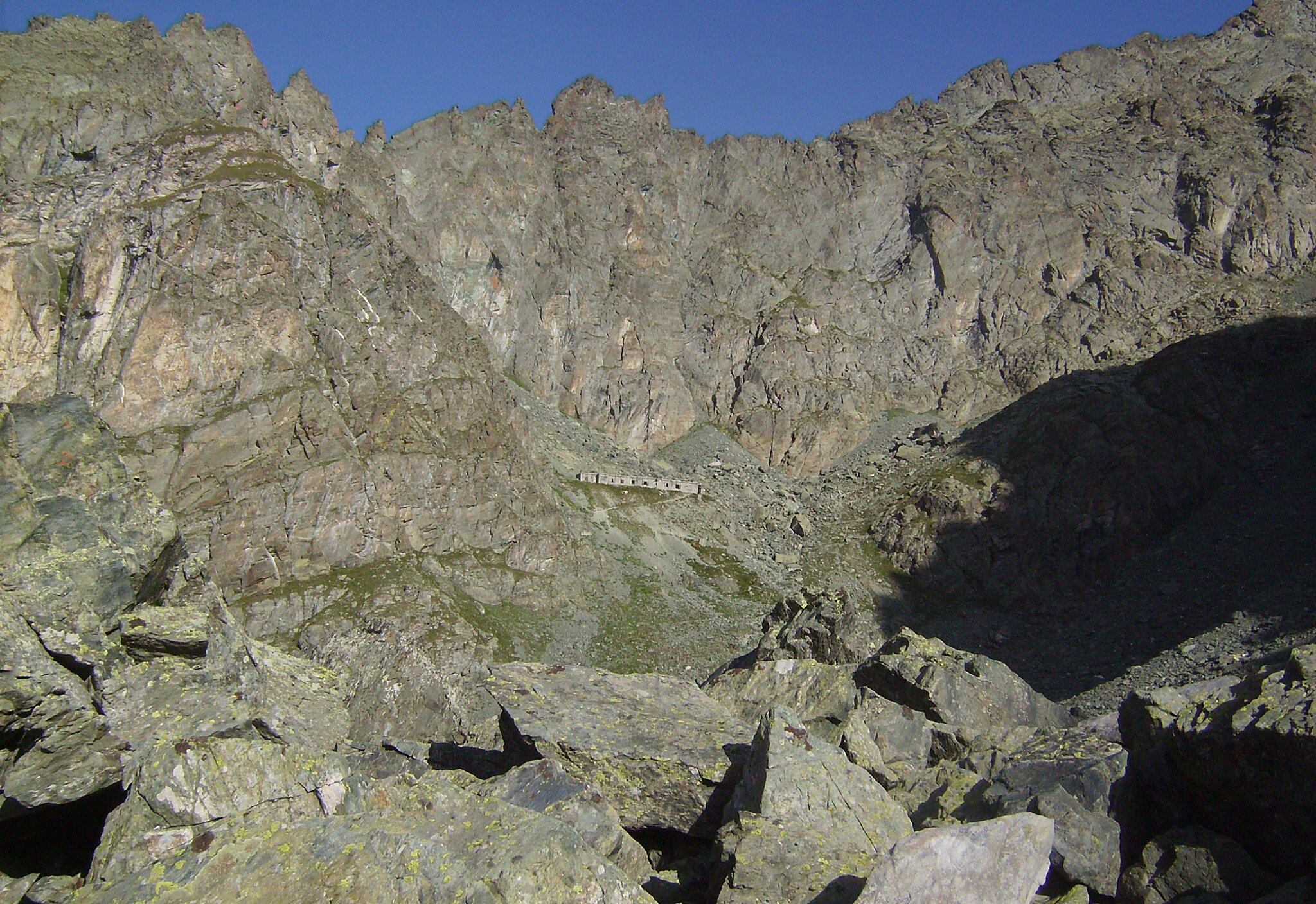 Ambiente montano roccioso con al centro in lontananza la caserma della traversette e sopra la catena montuosa che svetta.