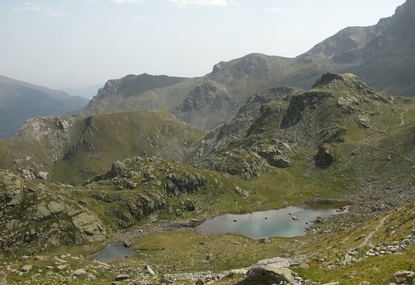 Due laghi alpini, a destra più grande e a sinistra una pozza più piccola in una conca erbosa con rocce. Intorno montagne
