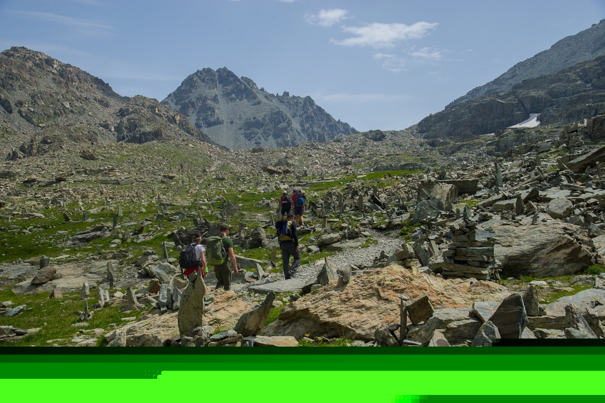sentiero montano tra prati verdi con molte pietre e rocce in equilibrio sul lato più stretto, cielo azzurro